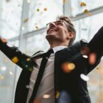 Happy businessman celebrating success with arms raised and confetti falling in modern office setting