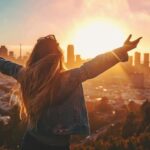 Woman celebrating with arms raised overlooking city skyline at sunrise