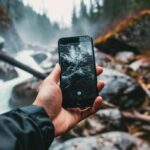 Hand holding smartphone with reflection of river and forest landscape on screen against misty woodland background