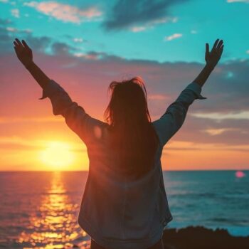 Woman raising arms in celebration at sunset by the sea