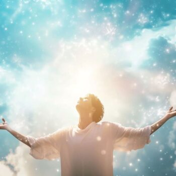 Man with arms raised towards the sky experiencing spiritual awakening or freedom with sparkling lights and clouds in the background.