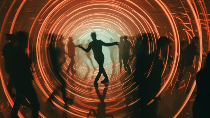 Silhouetted people dancing in a vibrant tunnel with dynamic orange light rings creating a sense of motion and energy.
