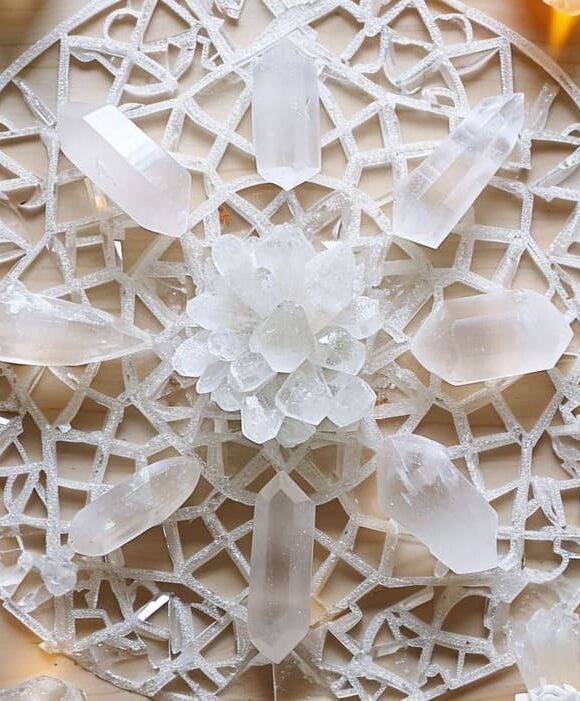 Intricate quartz crystal mandala with geometric patterns and crystal clusters on a wooden surface.