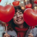 Happy woman holding heart-shaped balloons on Valentine's Day with blurred city lights background.