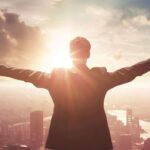Businessman with arms raised facing sunrise over city skyline expressing success and ambition
