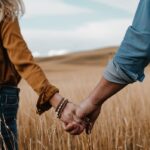 Couple holding hands in a golden wheat field with a blurred background