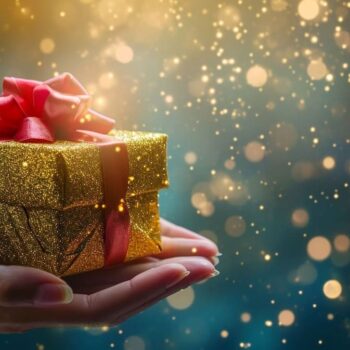 Hand presenting a glittery gold gift with red ribbon against a sparkling bokeh background