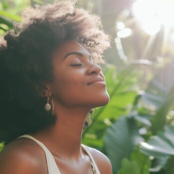 Young woman enjoying nature with eyes closed in sunlit tropical garden