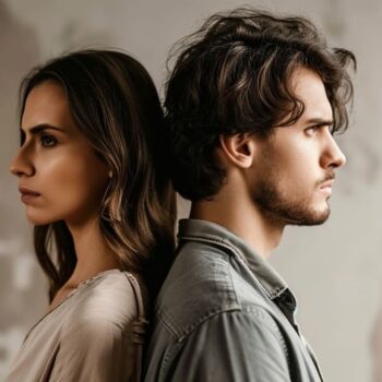 Side profile of a young man and woman standing back to back with serious expressions against a neutral backdrop.